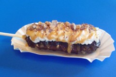 English Toffee Fudge Puppy -- Chocolate-covered bits of English toffee baked in the middle of a fudge puppy (Belgian waffle on-a-stick) then dipped in chocolate and layered with whipped cream, a toffee sauce and more bits of chocolate-covered English toffee. Available at Granny's Kitchen Fudge Puppies, located on the outside west wall of the Food Building. (Photo courtesy of the Minnesota State Fair.)